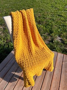 a yellow blanket sitting on top of a wooden floor next to a white chair and green grass