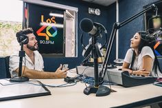 a man and woman sitting in front of microphones talking to each other on the radio