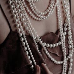 a close up of a person wearing pearls on their necklaces and holding something in her hand