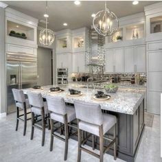 a large kitchen with an island and marble counter tops in front of stainless steel appliances