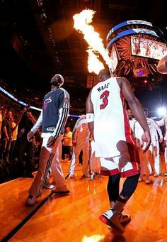 a group of men standing on top of a basketball court with fire in the air