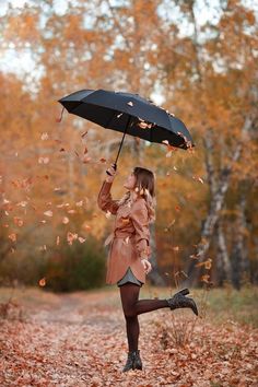 a woman is holding an umbrella in the air while falling leaves are all around her