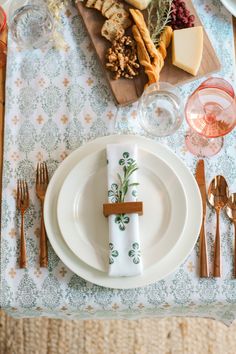 a place setting with silverware, napkins and wine glasses on a floral table cloth