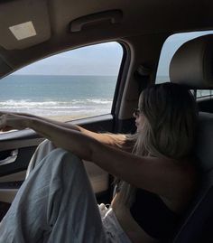 a woman sitting in the passenger seat of a car looking out at the ocean and beach