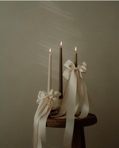 two candles with white ribbons and bows on a wooden table in front of a wall