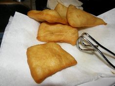 three pieces of fried food sitting on top of a white napkin next to a pair of tongs