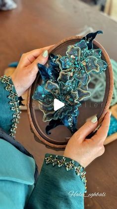 a woman holding a wooden bowl with blue flowers on it and beading in the middle