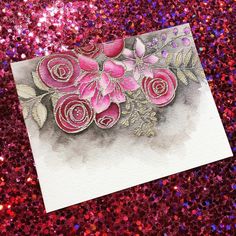 a card with pink flowers on it sitting on a glitter background and purple sequins