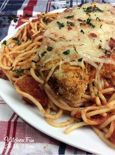 a white plate topped with spaghetti and meat covered in cheese sauce on top of a checkered table cloth