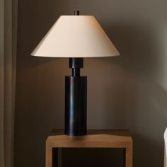 a table lamp sitting on top of a wooden table next to a white vase and wall