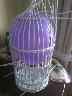 a purple ball in a white cage sitting on a table next to a plate and vase