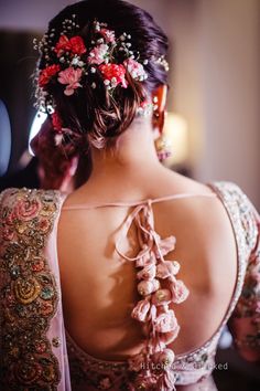 the back of a woman's head with flowers in her hair and jewelry on