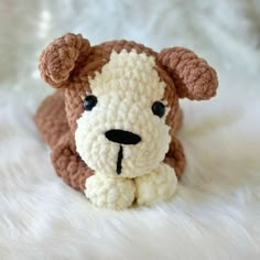 a crocheted dog is laying down on a white fur covered surface with it's eyes open