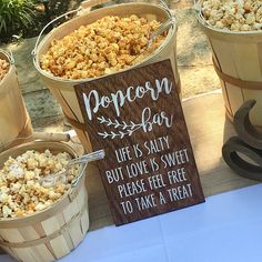 popcorn bar sign next to buckets of food on the table at an outdoor event