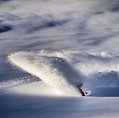 a man riding a snowboard down the side of a snow covered slope under a cloudy sky