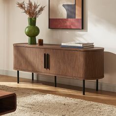 a living room with a large painting on the wall next to a wooden cabinet and coffee table