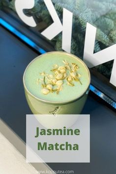 a cup filled with green liquid sitting on top of a table next to a window