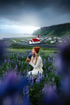 A woman smelling Lupine flowers at Vik in Iceland by a church. Linked to Visit Iceland's Vik Church Surrounded by a Field of Lupine Flowers. Renee Roaming, Perfect Bucket List, Lupine Flowers, Trip To Iceland