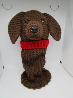 a knitted dog with a red collar on it's neck sitting in a white box