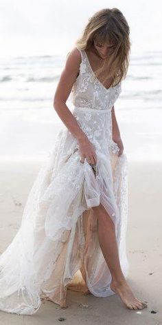 a woman standing on top of a sandy beach next to the ocean wearing a white dress