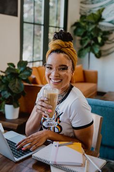 a woman sitting at a table with a glass of coffee in front of her laptop