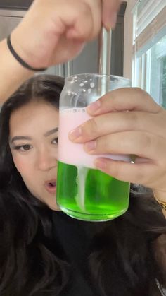 a woman holding up a green and pink drink