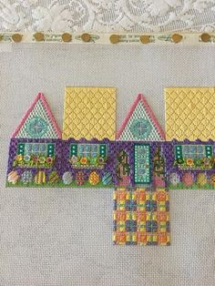 three small houses made out of different colors and patterns on a white tablecloth next to a lace doily