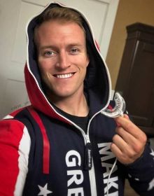 a man in a red, white and blue hoodie smiles while holding an object