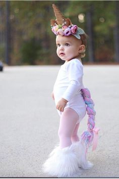 a baby girl wearing a unicorn outfit and holding a pony tail in the middle of an empty parking lot