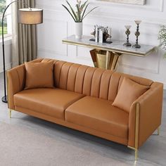 a tan leather couch sitting next to a table with a lamp on top of it