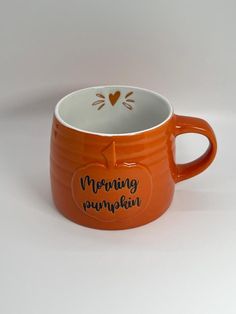 an orange coffee cup with a cat on the side and morning pumpkin written in black