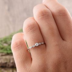 a woman's hand with a diamond ring on top of her finger and grass in the background