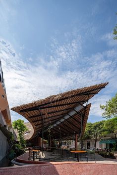 an outdoor covered area with tables and benches under a blue sky filled with white clouds