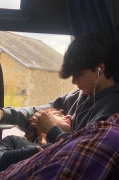 two people sitting in the back seat of a car, one is listening to headphones