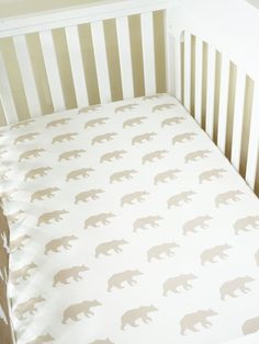 a white crib bed with brown bears on the sheets and bottom sheet in beige