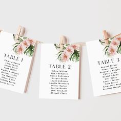 wedding seating cards hanging on clothes pins with pink flowers and greenery in the center