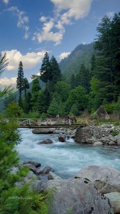 people are walking across a bridge over a river in the mountains with rocks and trees