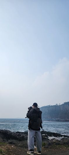 a man standing on top of a beach next to the ocean with a kite flying in the sky