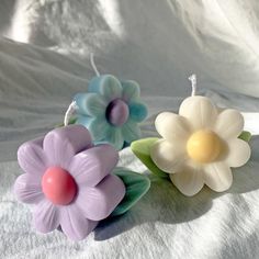 three flower shaped candles sitting on top of a white cloth covered tablecloth, with one candle in the shape of a flower