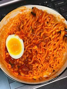 a plate of noodles and an egg on top of the computer keyboard, ready to be eaten