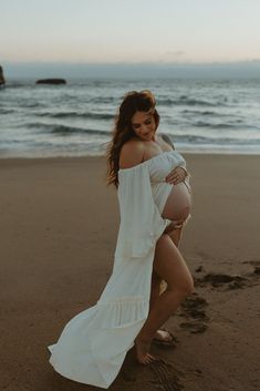 a pregnant woman is standing on the beach