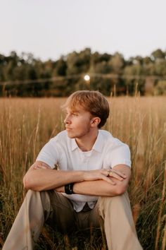 a man sitting in the middle of a field with his arms crossed and looking off into the distance