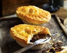 two pies sitting on top of a wooden table next to a knife and fork