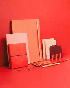 three notebooks and two pens are on a red surface next to an orange book