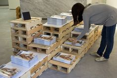 a woman bending over looking at books on wooden pallets