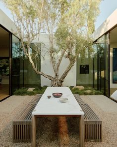 a table and chair in front of a tree with glass doors on the outside wall