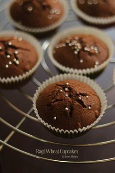 six chocolate cupcakes with white sprinkles on them sitting on a cooling rack