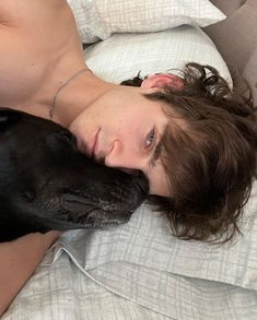 a person laying in bed with a dog on their lap and his head resting on the pillow