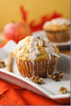 two muffins with icing and walnuts on a plate next to an apple