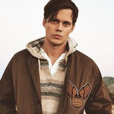 a young man wearing a brown jacket with an eagle patch on the front and chest